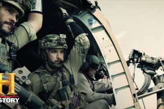 Two Navy SEAL operators in full tactical gear riding in a military helicopter, focused on their mission