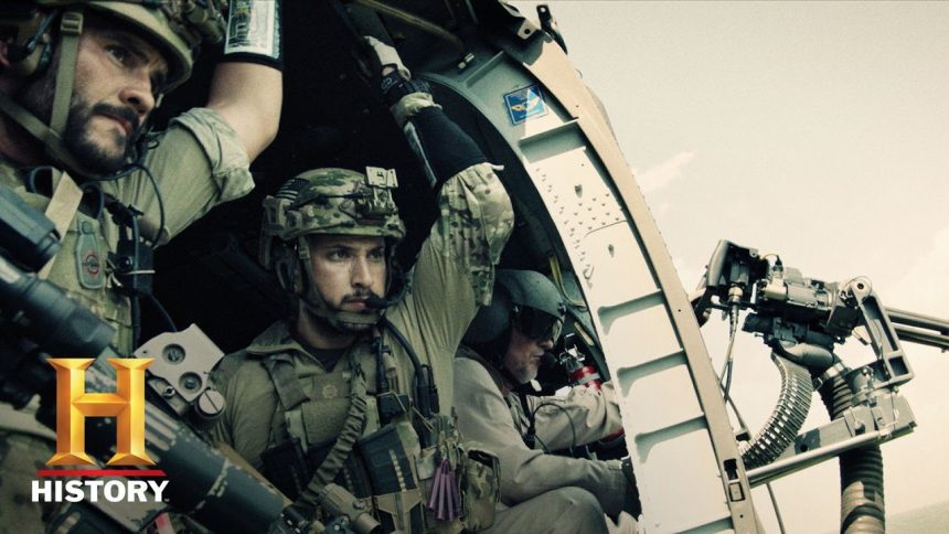 Two Navy SEAL operators in full tactical gear riding in a military helicopter, focused on their mission