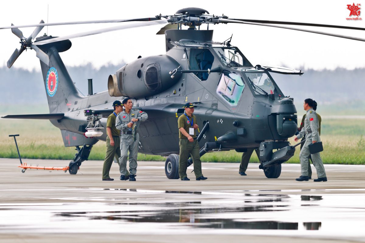 Parked CAIC Z-10 attack helicopter with armed ground crew performing maintenance checks on airstrip